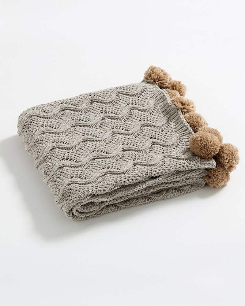 Plaid gris replié montrant les pompons marron
