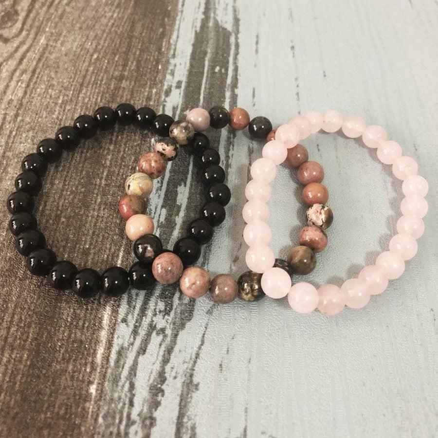 Trois bracelets en quartz rose, onyx et rhodonite sur fond blanc