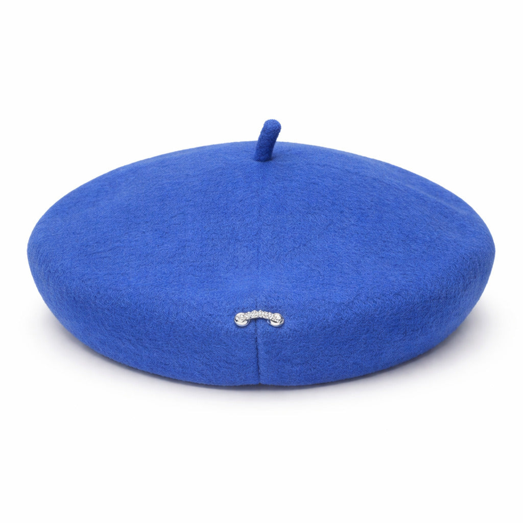 Béret posé sur une table, broche argentée en gros plan