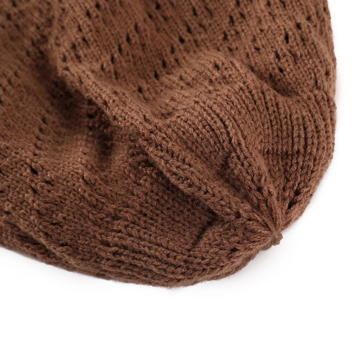 Bonnet tricoté ajouré rose posé sur une table en bois