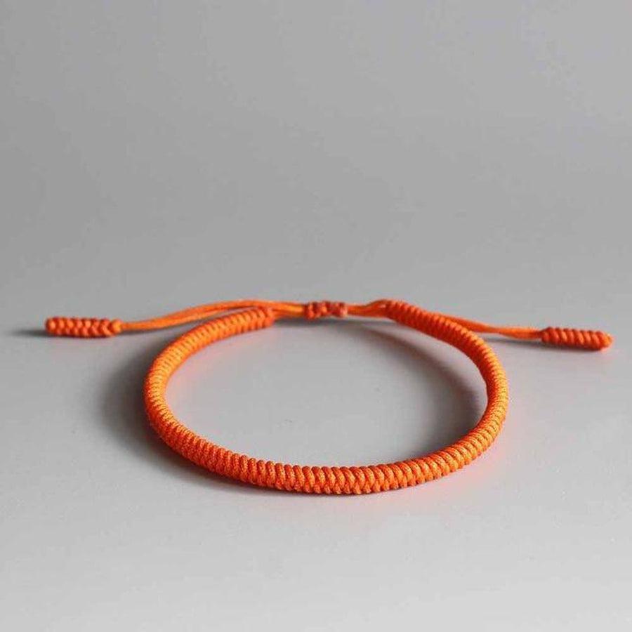 Bracelet bouddhiste en corde orange posé sur une surface