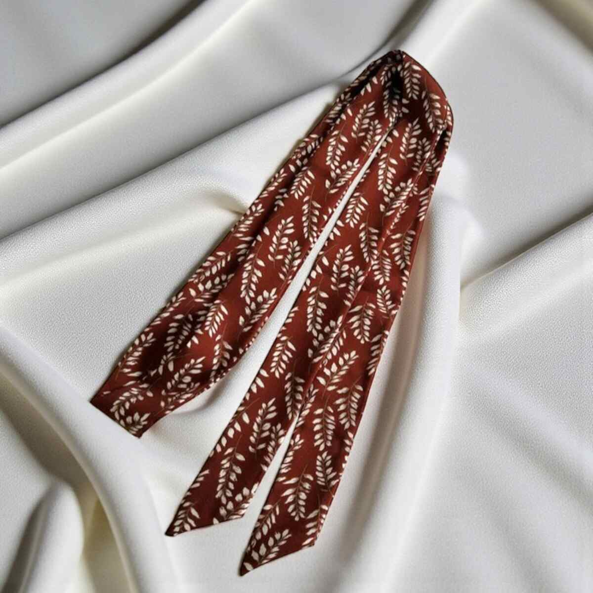 Ceinture foulard bordeaux posée sur une surface blanche
