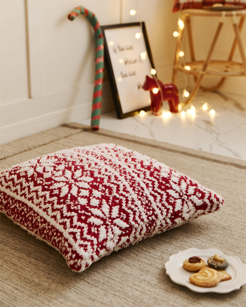 Coussin rouge avec motifs flocons blancs sur canapé neutre