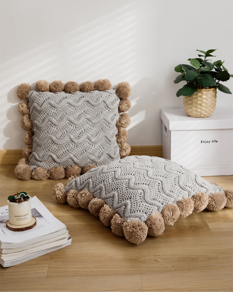 Coussin gris avec pompons marron sur canapé beige