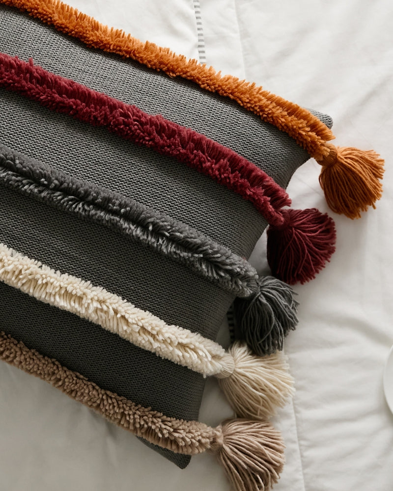 Coussin bohème gris avec pompons colorés aux extrémités