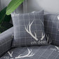 Deux housses de coussin extensibles, motif cerf, sur canapé gris