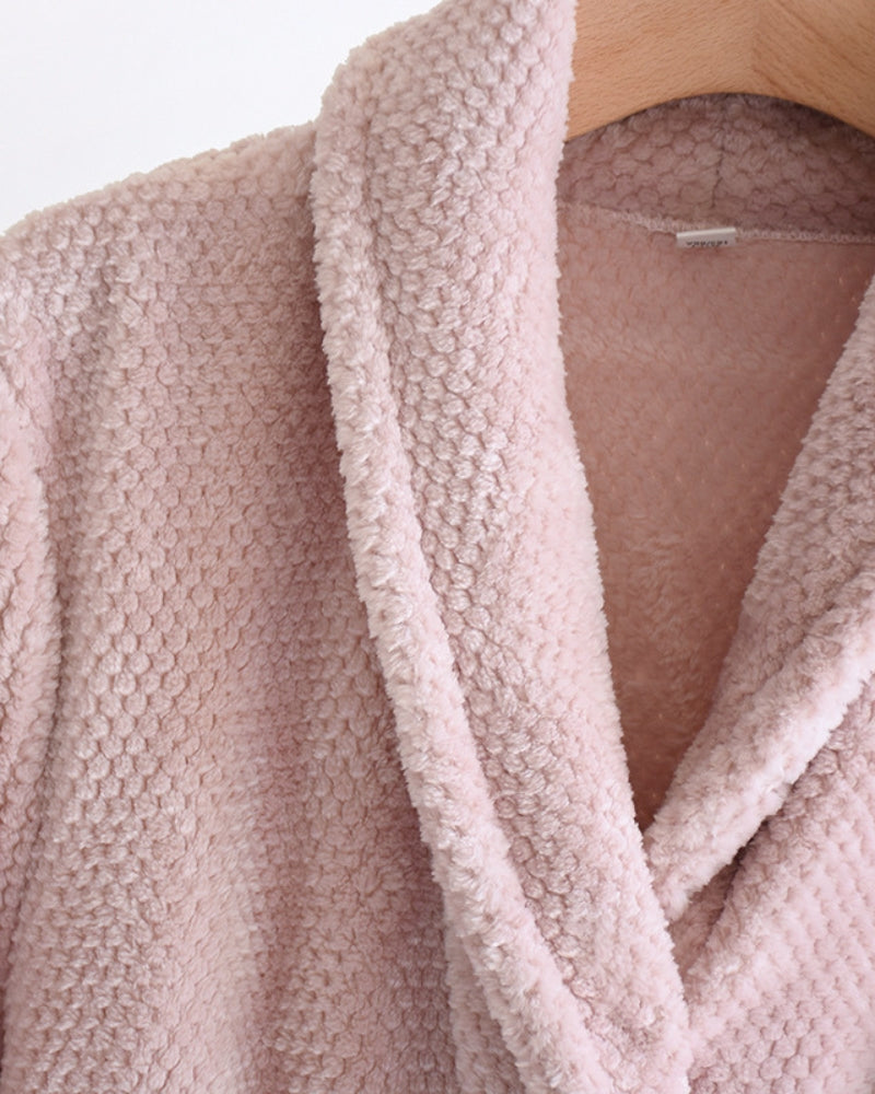 Peignoir doux rose posé sur un lit blanc
