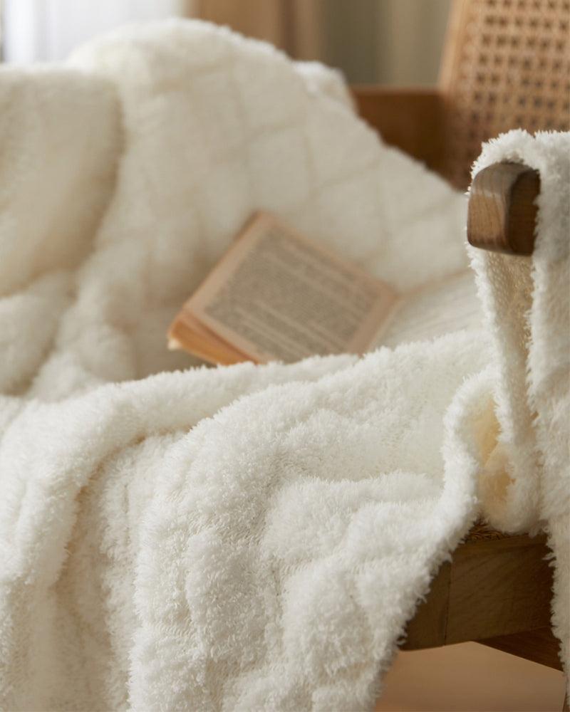 Plaid blanc plié sur un lit, ambiance cocooning