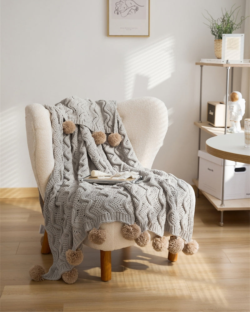 Plaid gris avec pompons marron sur canapé crème