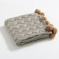 Plaid gris replié montrant les pompons marron